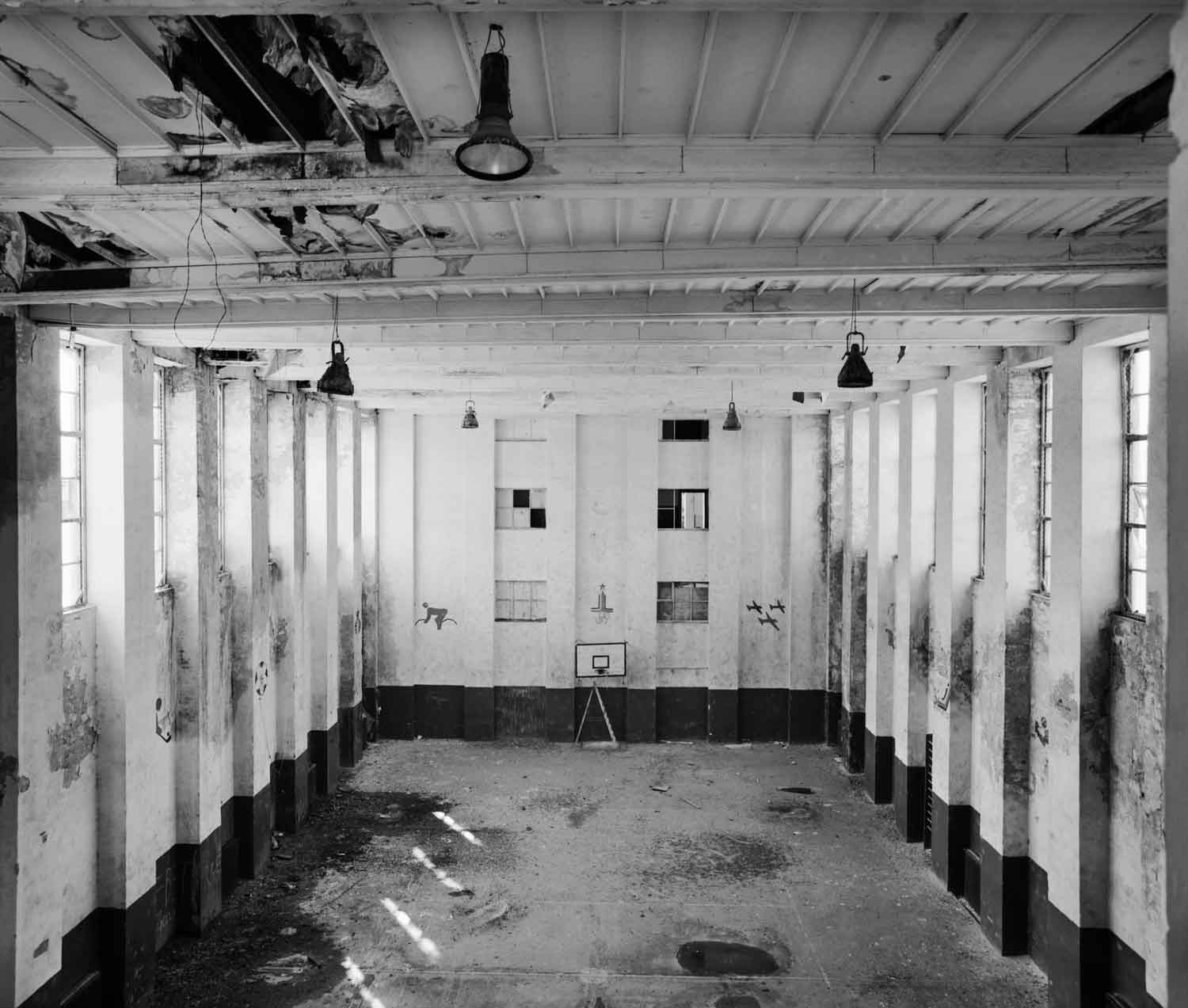 Foto, schwarz-weiß: Blick in den hinteren Teil des als Turnhalle genutzten Festsaals mit starken Abnutzungsspuren an den Wänden.