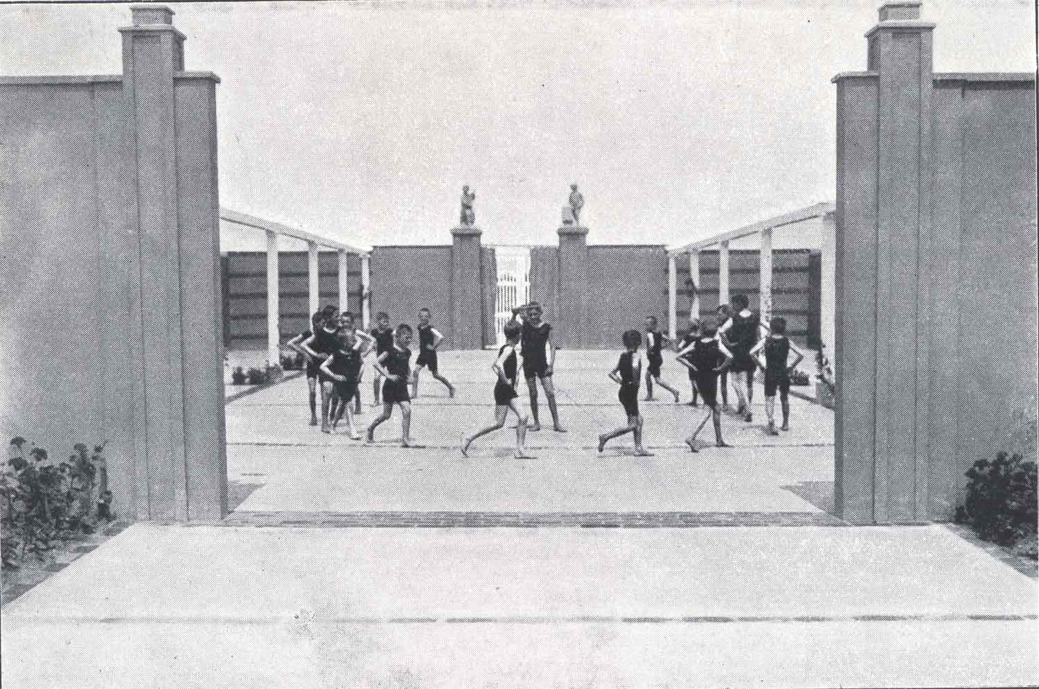 Foto, schwarz-weiß, außen: Eine Gruppe von Menschen in schwarzen Turnanzügen läuft in einem von Mauern eingefassten Areal im Kreis