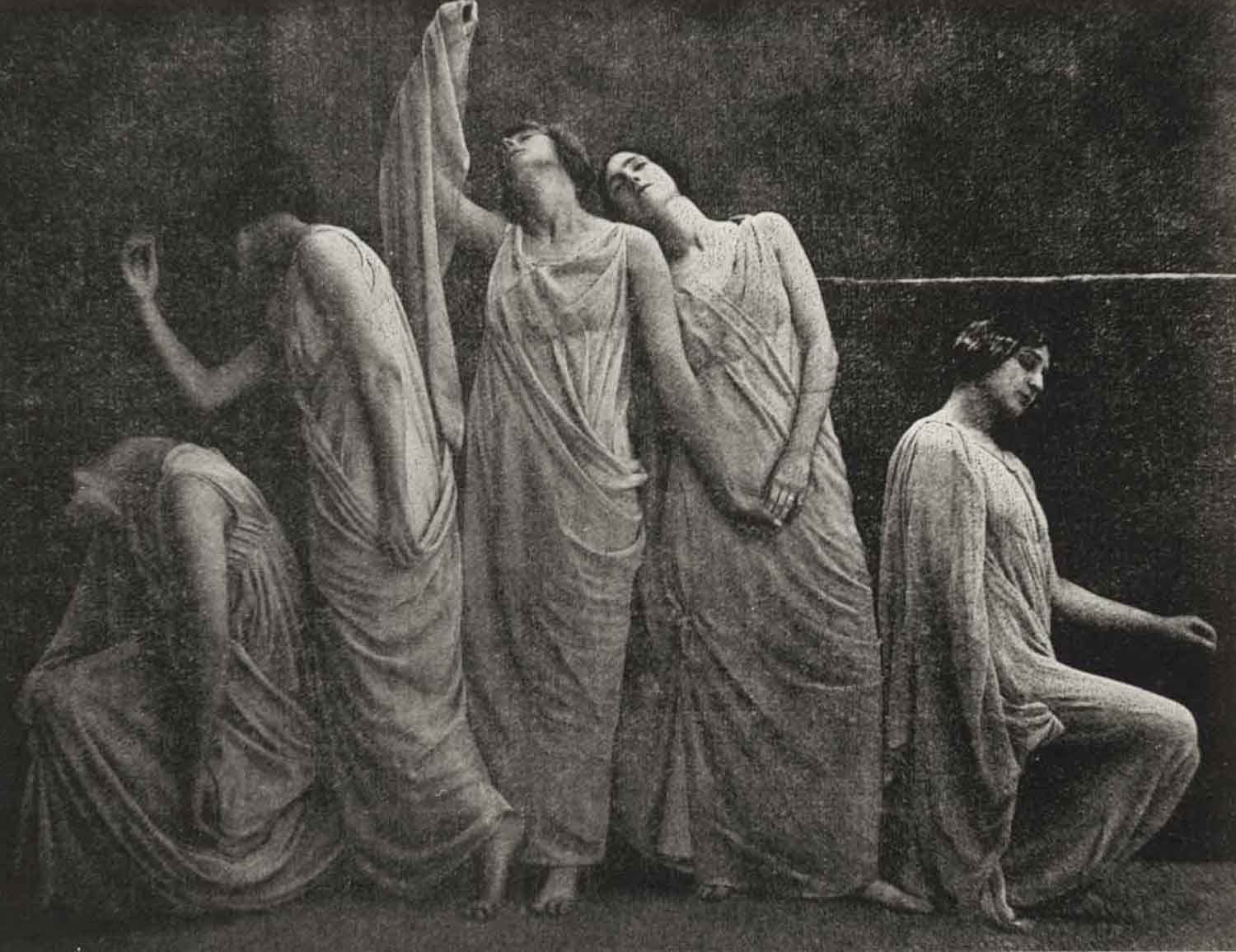 Foto, schwarz-weiß, innen: Fünf Frauen in weißen langen Kleidern hocken und stehen aneinandergelehnt in einer Reihe.