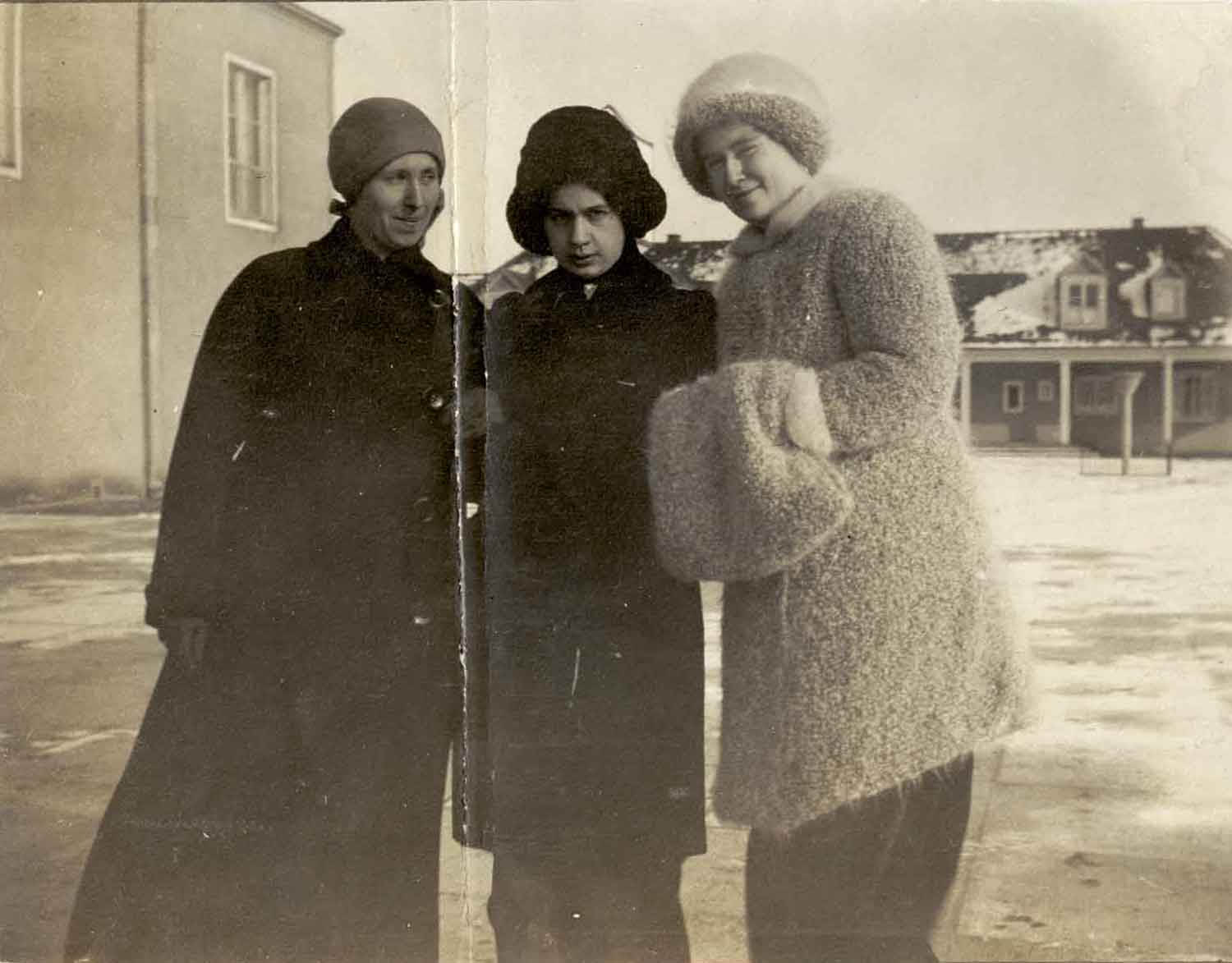 Foto, schwarz-weiß, außen: Drei Frauen mit Mützen in dicken Mänteln, zwei haben einen großen Pelz-Muff.