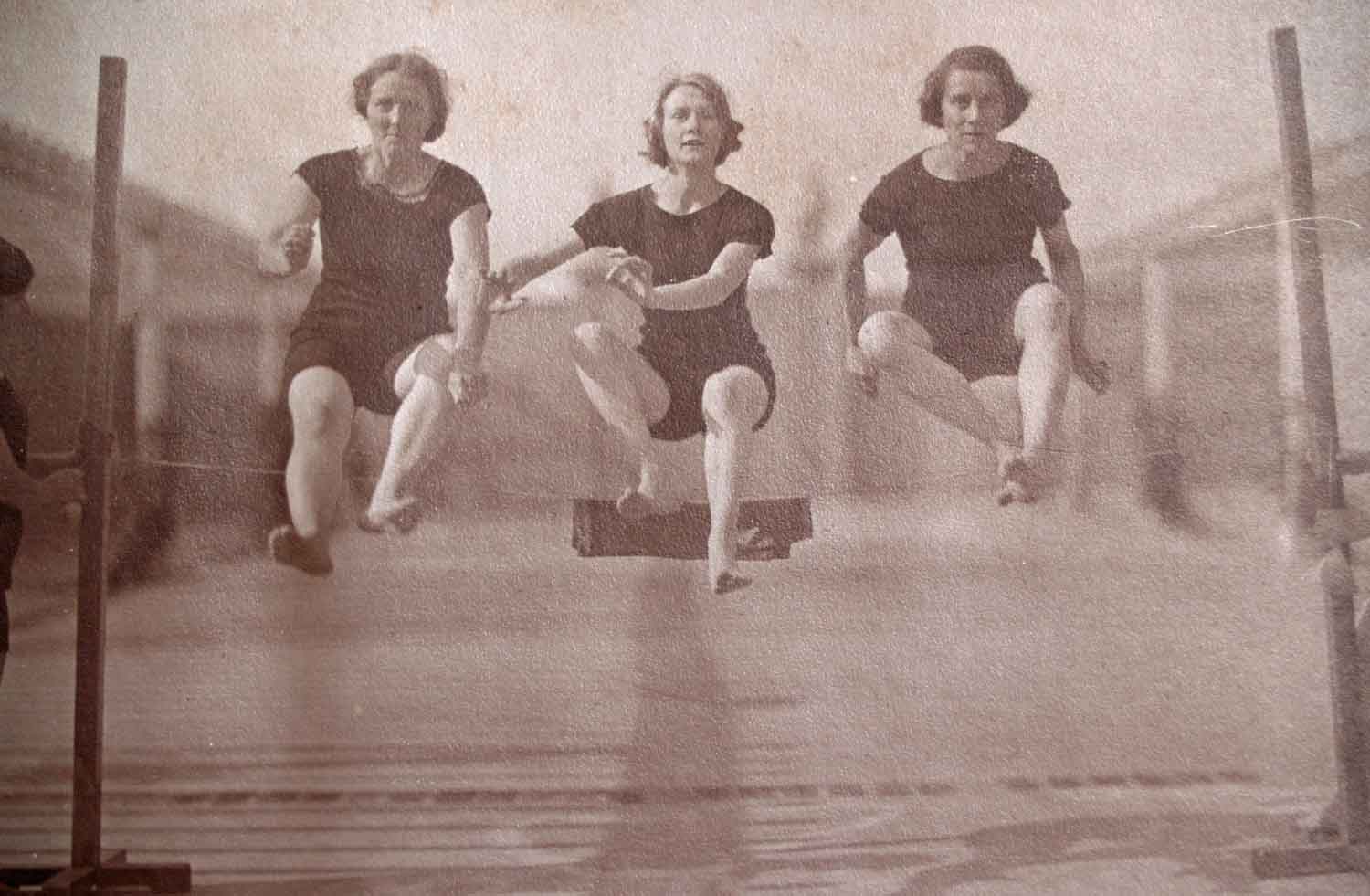 Foto, schwarz-weiß, außen: Drei Frauen in schwarzen Turnanzügen springen in die Luft.