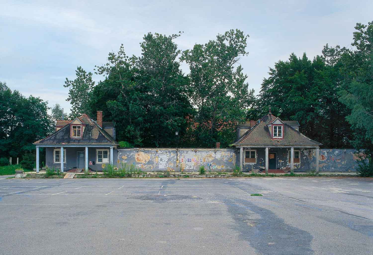 Foto, farbig, außen: Frontalansicht der grau getünchten Gebäude mit zahlreichen Schäden am Außenputz.